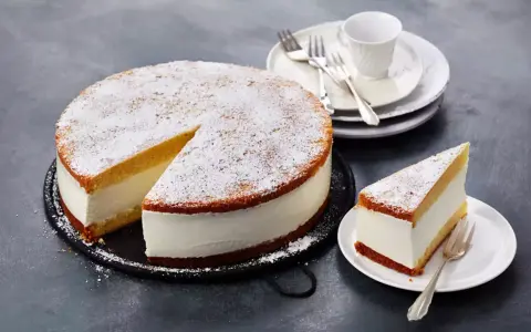 Eine köstliche Quark Sahne Torte, bestäubt mit Puderzucker, wartet darauf, genossen zu werden. Ein Stück ist bereits auf einem Teller angerichtet.
