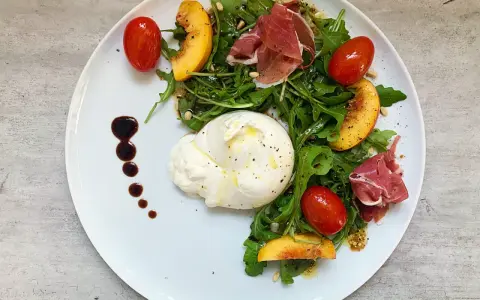 Salat mit Nektarinen, Burrata, Prosciutto und Kirschtomaten, garniert mit Balsamico-Dressing.