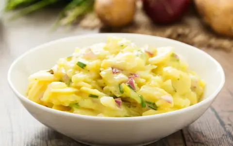 Omas Kartoffelsalat Rezept Original: Ein cremiger Kartoffelsalat mit Zwiebeln und Schnittlauch in einer weißen Schüssel, bereit zum Genießen.