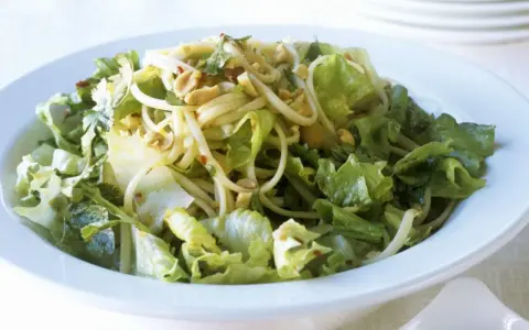 Ein leckerer Yum Yum Salat mit knackigem Eisbergsalat, Nudeln und Erdnüssen in einer weißen Schüssel.
