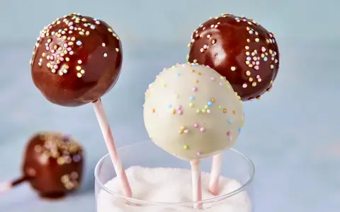 Drei bunte cake pops aus kuchenresten, mit Schokolade und Streuseln verziert, stecken in einem Glas voller Zucker.