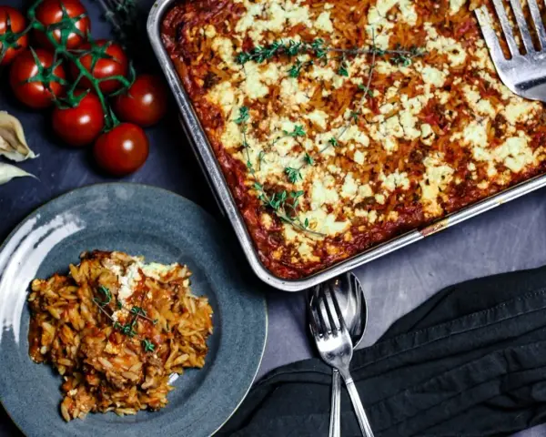 Herzhafter Kritharaki Auflauf mit Hackfleisch und Feta, garniert mit Thymian. Daneben frische Tomaten und Knoblauch.