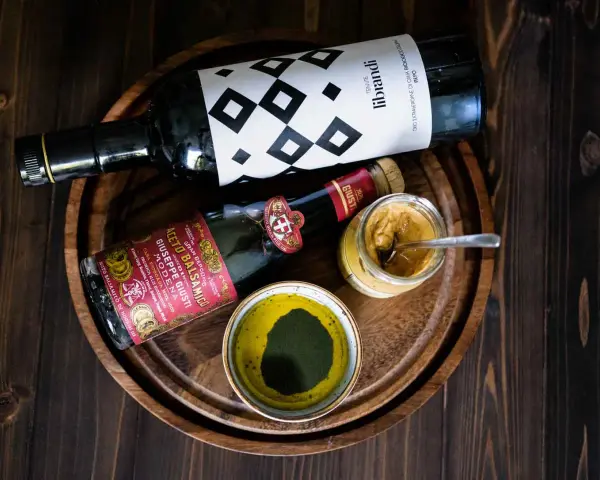 Zutaten für ein köstliches Balsamico-Dressing: eine Flasche Olivenöl, eine Flasche Aceto Balsamico Giuseppe Giusti und eine Schale mit grünen Kräutern.