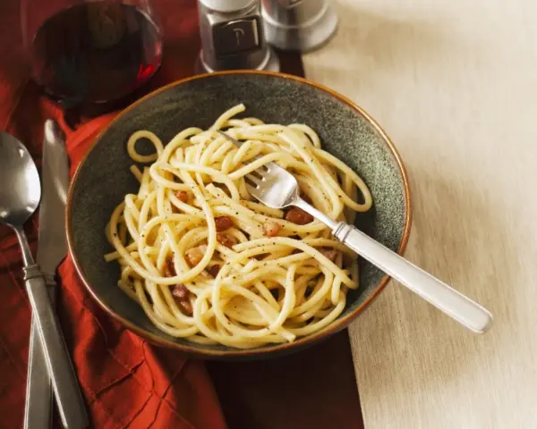 Eine Schüssel Spaghetti mit Speck und Pfeffer, eine köstliche Carbonara ohne Ei, serviert mit einem Glas Rotwein.