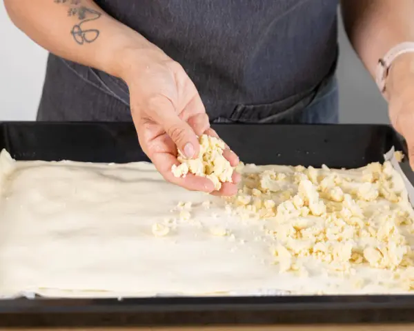 Hände verteilen Streusel auf einem Teigboden für ein Prasselkuchen Rezept DDR.