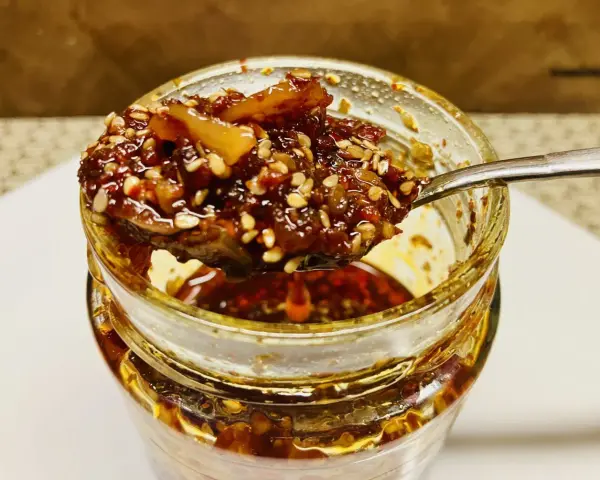 Ein Löffel voller knusprigem Chiliöl mit Sesam und Gewürzen, bereit, Gerichte zu verfeinern.