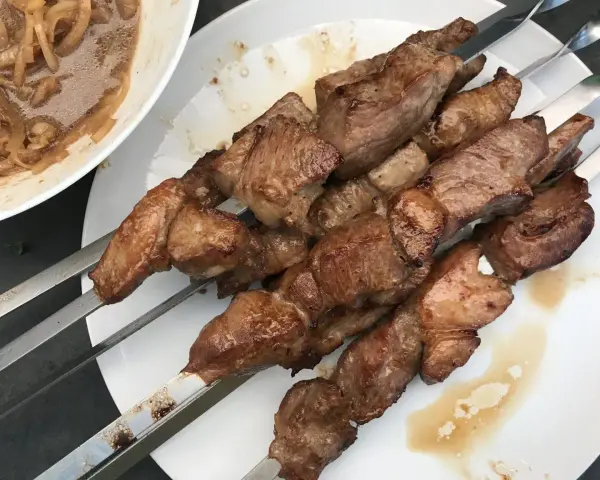 Saftige Fleischspieße, perfekt gegrillt, wie beim besten russischen Schaschlik Rezept. Dazu eine Schüssel mit marinierten Zwiebeln.
