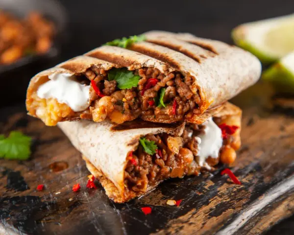 Zwei saftige Burritos, gefüllt mit Hackfleisch, Bohnen und einem Klecks Sauerrahm, sind ein köstliches burrito rezept. Garniert mit Koriander und Chili.