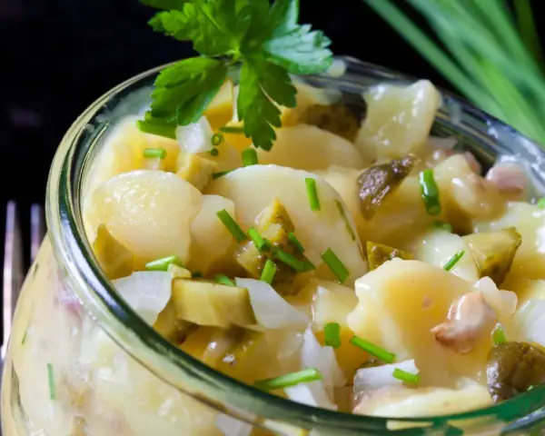 Ein köstlicher Kartoffelsalat ohne Mayo, mit Gurken, Zwiebeln und frischen Kräutern, serviert in einem Glas.