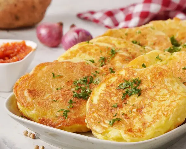 Goldbraune Kartoffelpuffer, garniert mit Petersilie, sind ein köstliches Beispiel für Rezepte mit Kartoffeln als Hauptspeise. Dazu passen Tomatensoße und Zwiebeln.