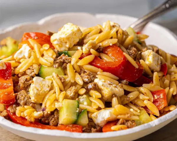 Herzhafter Kritharaki Salat mit Hackfleisch, Feta, Gurke und roten Paprikastücken. Ein köstliches Gericht, das alle Geschmacksnerven verwöhnt.