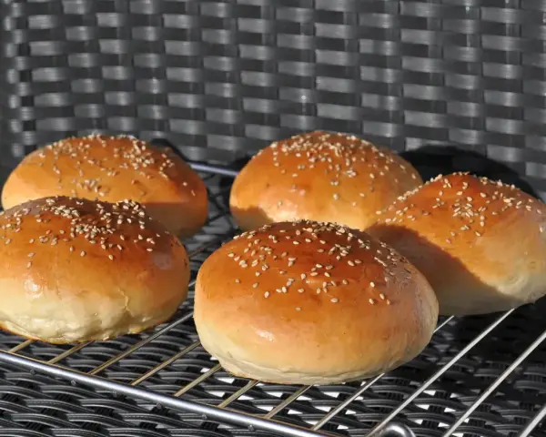 Fünf goldbraune Burgerbrötchen mit Sesam, frisch gebacken nach einem tollen burger buns rezept.