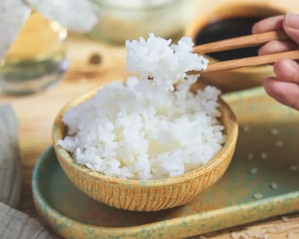 Perfekter sushi reis im reiskocher, dampfend und bereit, mit Stäbchen gegriffen zu werden. Ein Hauch von Asien auf dem Tisch.
