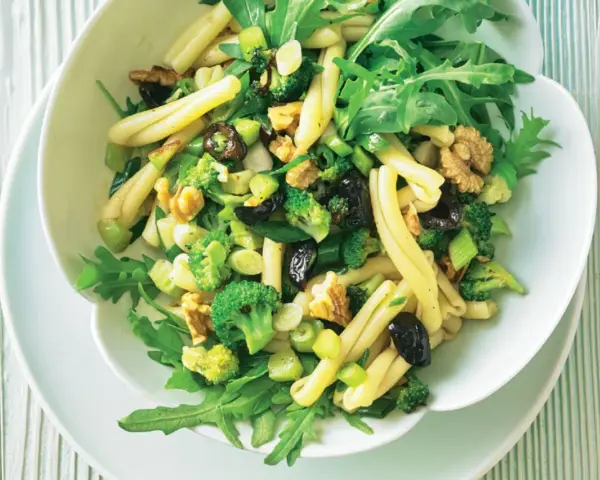 Frischer nudelsalat mit brokkoli, Walnüssen, Oliven und Rucola in einer weißen Schüssel.