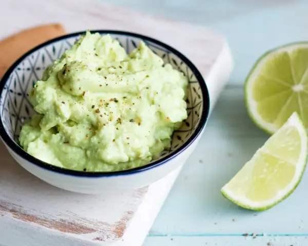 Cremiger Avocado Feta Dip, gewürzt mit Pfeffer, daneben frische Limettenspalten. Perfekt zum Dippen!