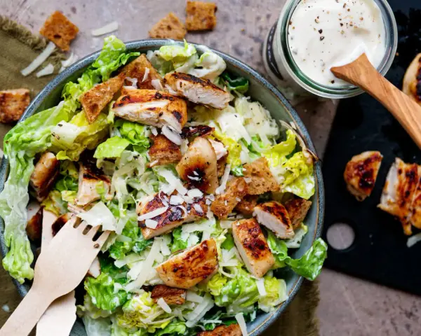 Frischer Caesar Salat mit gegrilltem Hähnchen, Croutons und Parmesan. Dazu ein Glas mit cremigem Caesar Salat Dressing.