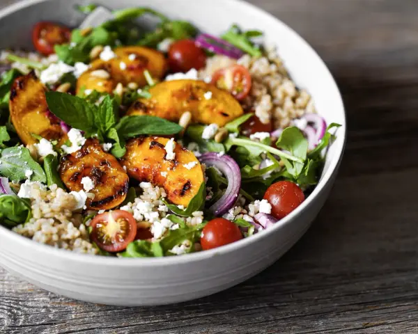 Ein bunter Pfirsich Feta Salat mit gegrillten Pfirsichspalten, Kirschtomaten, Rucola und Getreide.