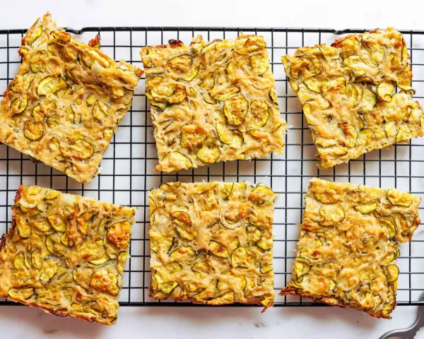 Sechs rechteckige Stücke Zucchini Scarpaccia liegen auf einem schwarzen Gitterrost.