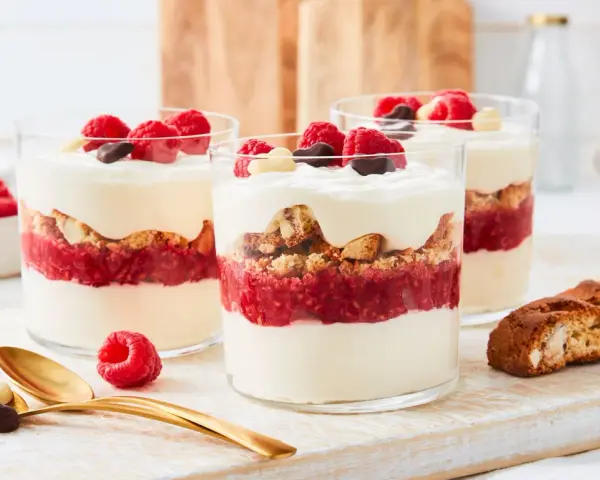 Schichtdessert mit Himbeeren, knusprigen Keksen und cremigem **dessert mit mascarpone**, garniert mit frischen Beeren und Schokolade.