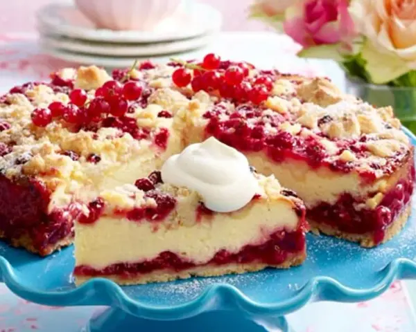 Saftiger Johannisbeerkuchen mit Quark und Streuseln, garniert mit frischen roten Johannisbeeren und einem Klecks Sahne.