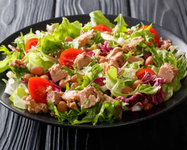 Frischer Thunfischsalat mit knackigem Salat, Tomaten und Bohnen auf schwarzem Teller.