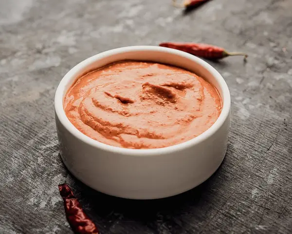 Eine Schale mit cremiger Piri Piri Sauce, umgeben von getrockneten Chilis auf dunklem Untergrund.