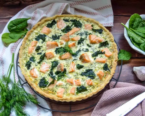 Herzhafte Spinat Lachs Quiche mit frischem Dill garniert, bereit zum Servieren.
