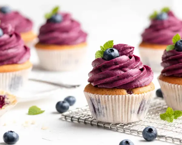 Mehrere Muffins mit lila Beeren-Topping, garniert mit frischen Blaubeeren und Minze. Ein einfacher, köstlicher Genuss.