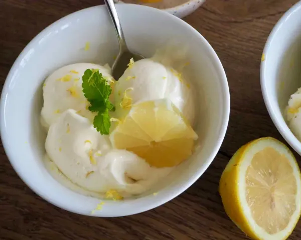 Erfrischendes zitroneneis selber machen: Cremiges Eis in einer Schüssel, garniert mit Zitronenspalte und Minze.
