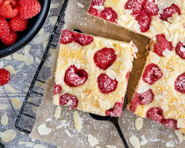 Schneller Kuchen mit gefrorenen Himbeeren, bestreut mit Puderzucker und Mandelblättchen. Ein Genuss für jeden Anlass!