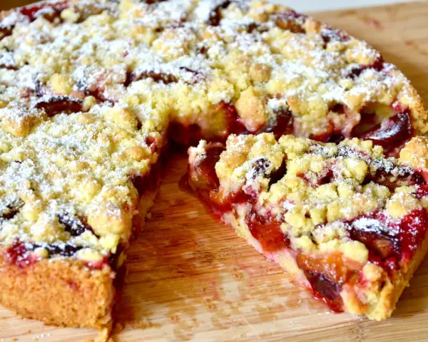 Saftiger pflaumenkuchen ohne hefe springform, mit Streuseln und Puderzucker bestäubt, auf einem Holzbrett.