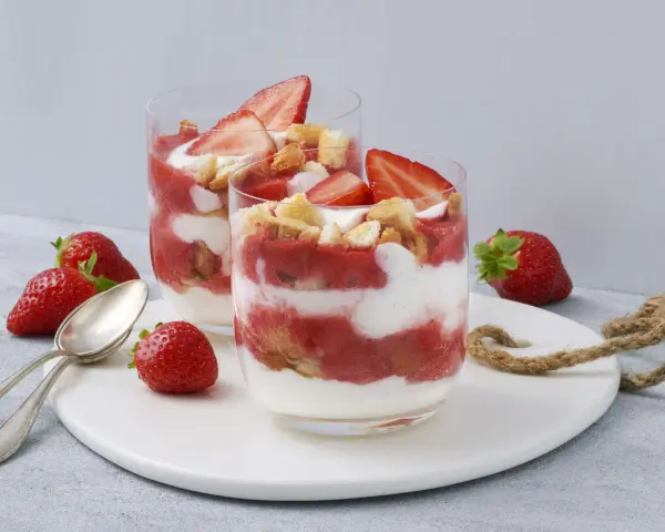 Zwei Gläser mit einem sommerlichen Dessert aus Erdbeeren und Sahne, garniert mit frischen Erdbeeren und Keksen. Ein schnell und einfach zubereitetes Genusserlebnis.