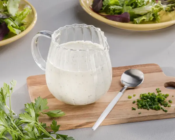 Ein Krug mit cremigem Ranch Dressing, daneben Schnittlauch und Petersilie. Perfekt für einen frischen Salat.