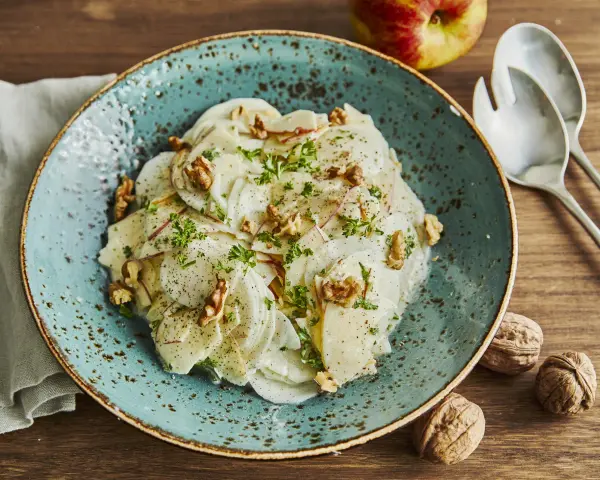 Ein erfrischender rettichsalat mit apfel, garniert mit Walnüssen und Petersilie, auf einem türkisfarbenen Teller.
