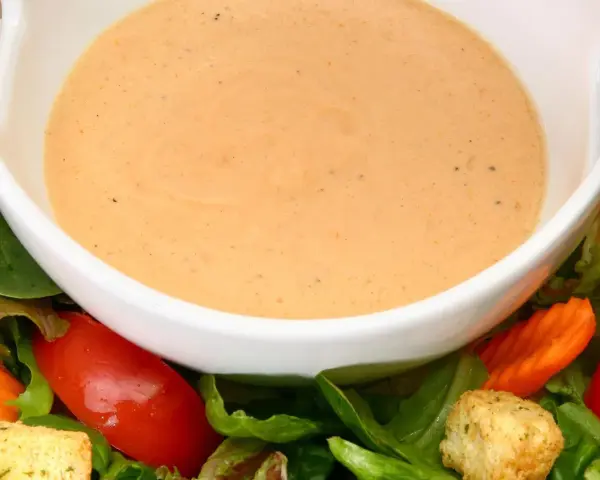 Cremiges French Dressing in einer weißen Schüssel, umgeben von frischem Salat, Tomaten und Karotten.