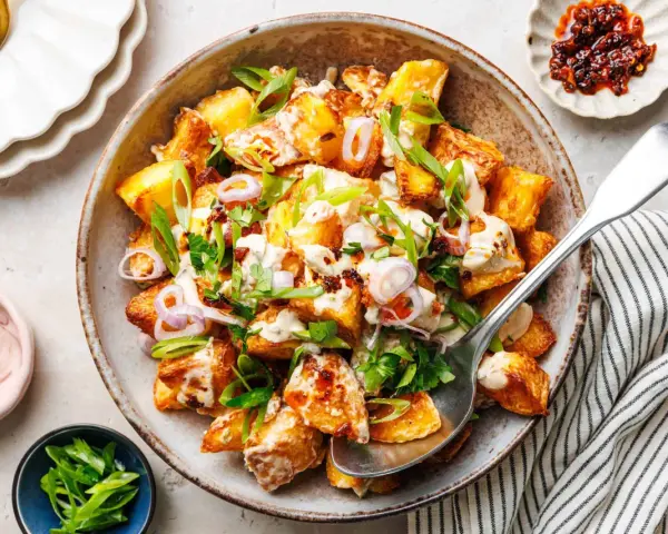 Kartoffelsalat mal anders: knusprige Kartoffelspalten mit cremiger Sauce, Frühlingszwiebeln und roten Zwiebelringen in einer rustikalen Schüssel.