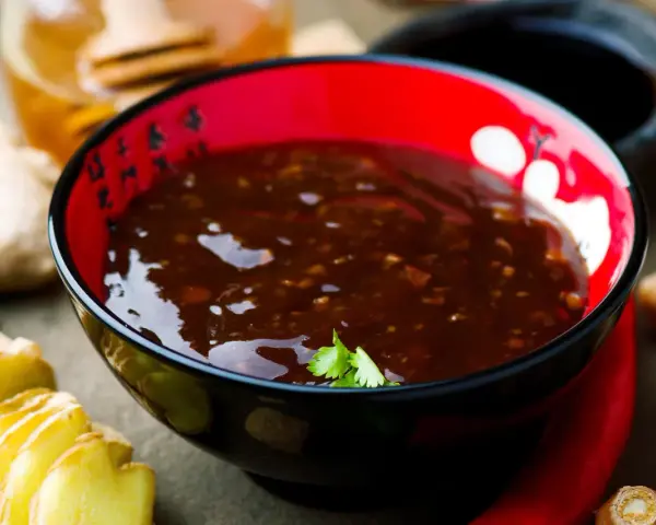 Schwarze Schüssel mit glänzender Teriyaki-Sauce, umgeben von Ingwer, Knoblauch und Chili. Ein köstliches teriyaki sauce rezept zum Nachkochen.