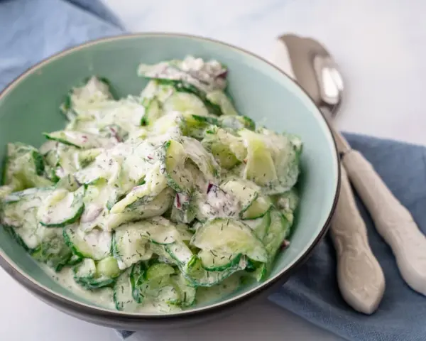 Frischer gurkensalat mit saurer sahne, garniert mit Dill und roten Zwiebeln, serviert in einer hellgrünen Schüssel.
