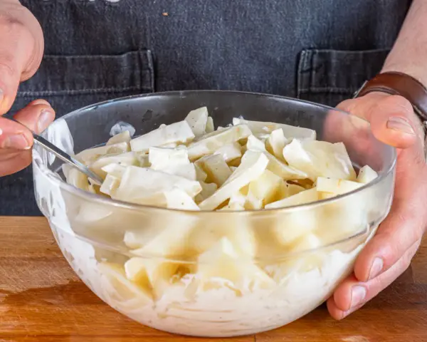 Hände mischen in einer Glasschüssel den cremigen selleriesalat nach Omas Rezept.