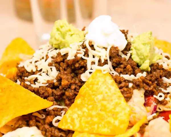 Schichtsalat mit Hackfleisch, Käse, Guacamole und saurer Sahne, garniert mit knusprigen Nachos.
