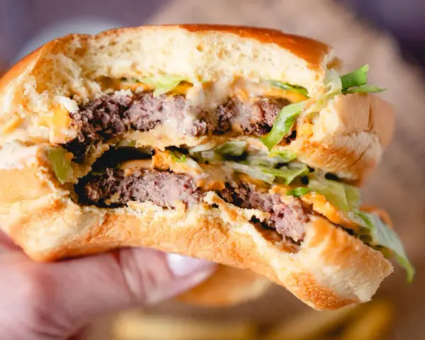 Ein saftiger Burger mit zwei Rindfleisch-Patties, Salat und der unverwechselbaren Big Mac Sauce, gehalten in einer Hand.