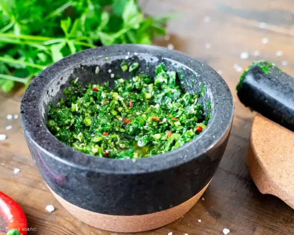 Frisches Chimichurri-Rezept im Mörser, bereit zum Verfeinern von Grillgut. Kräuter, Chili und Gewürze sind fein gehackt.
