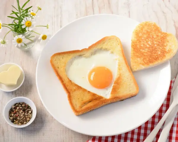 Herzförmiger Toast mit Ei, daneben ein Herzbutterstück und ein Herz-Toast. Ein liebevolles Frühstück.
