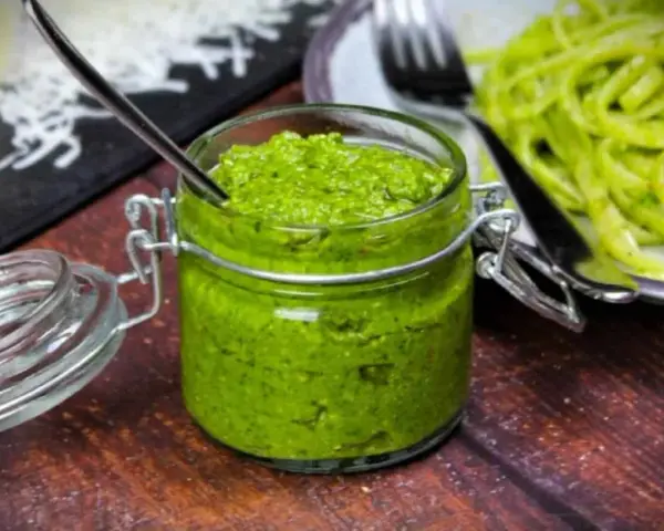 Frisches Rucola Pesto in einem Glas mit Löffel, daneben Pasta.