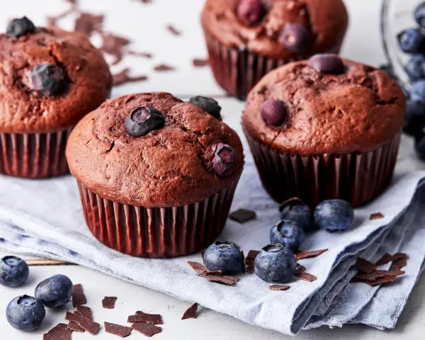 Saftige schoko blaubeer muffins, garniert mit frischen Blaubeeren und Schokostückchen, liegen auf einem Leinentuch.