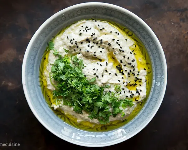 Cremiges Baba Ganoush, beträufelt mit Olivenöl, garniert mit frischer Petersilie und schwarzen Sesamkörnern.