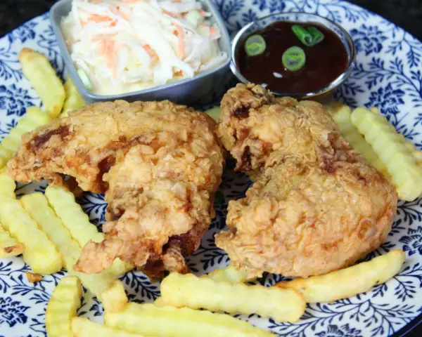 Knusprige chicken wings mit Pommes, Cole Slaw und BBQ-Sauce auf einem blau-weißen Teller.