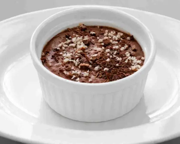 Ein cremiges Mousse au Chocolat, garniert mit Schokoladenraspeln und feinen Salzkristallen, serviert in einer weißen Schale auf einem Teller.