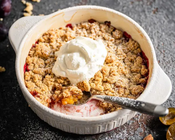 Ein köstlicher Zwetschgen Crumble mit Haferflocken, gekrönt mit einem Klecks Sahne, wartet darauf, genossen zu werden.