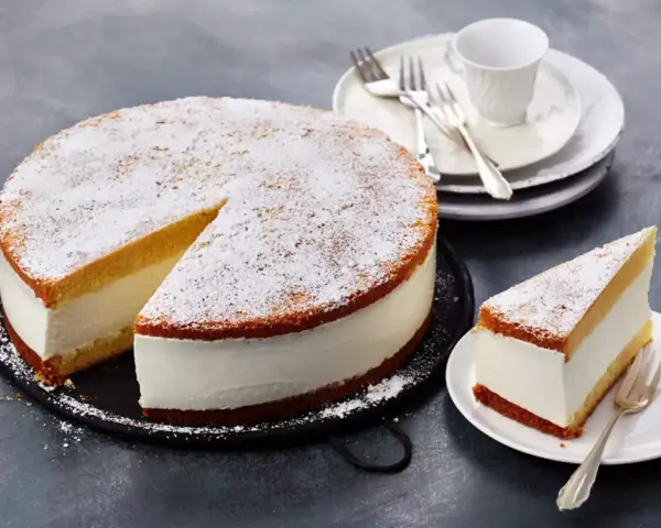 Eine köstliche Quark Sahne Torte, bestäubt mit Puderzucker, wartet darauf, genossen zu werden. Ein Stück ist bereits auf einem Teller angerichtet.
